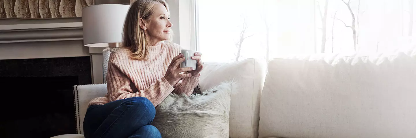 Frau sitz mit einer Tasse am Fenster