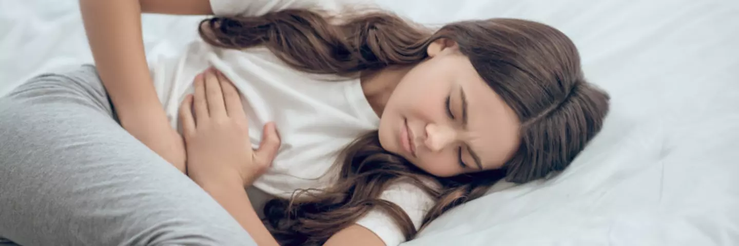Mädchen liegt mit Bauchschmerzen im Bett