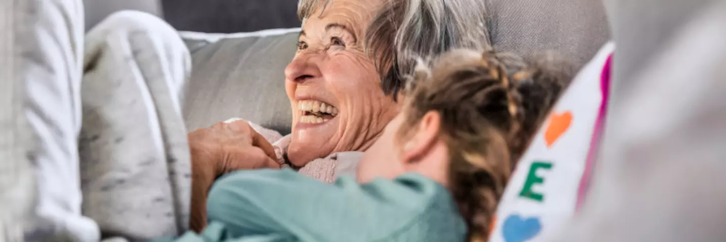 Seniorin sitzt lachend mit Enkelin auf der Couch