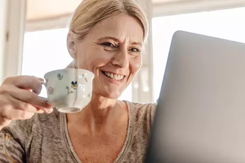 Frau sitzt mit Kaffeetasse am Laptop