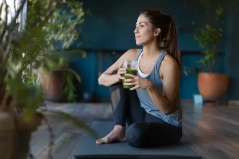 Frau sitzt auf einer Yoga-Matte und trinkt einen Smoothie