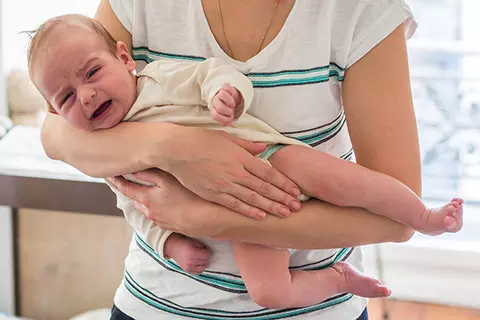 Eine Mutter mit Baby, hält das Baby im Fliegergriff, weil dieses unter starken Blähungen leidet.