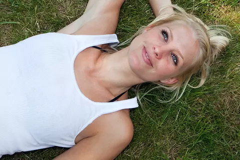 Eine junge Frau liegt auf der Wiese und hat ihre Bauchbeschwerden (Blähungen) im Griff.
