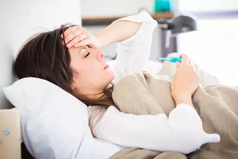 Eine Frau mit einem grippalen Infekt und Fieber liegt im Bett.