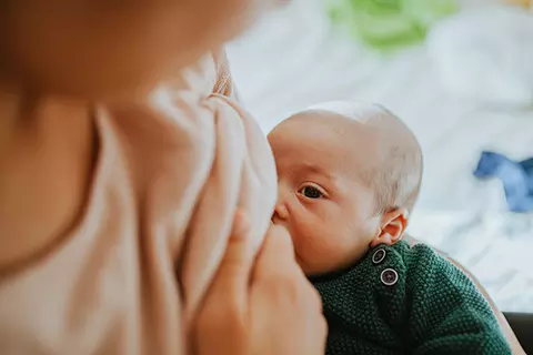 Eine junge Mutter stillt ihr Baby, das an einem grippalen Infekt erkrankt ist.