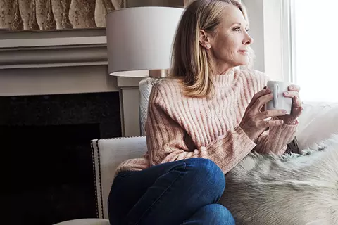 Frau sitz mit einer Tasse am Fenster