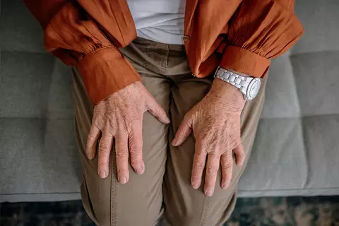 SeniorInn sitzt mit den Händen auf den Knien auf der Couch