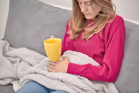 Frau mit Blasenentzündung sitzt mit einer Decke und einer Tasse Tee auf der Coucht