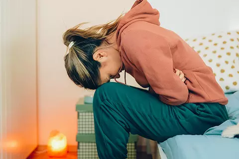 Frau krümmt sich mit Schmerzen auf dem Bett