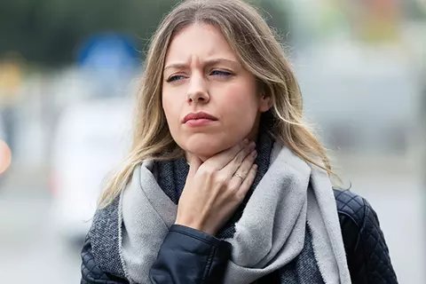 Frau hält sich mit leidendem Blick den Hals