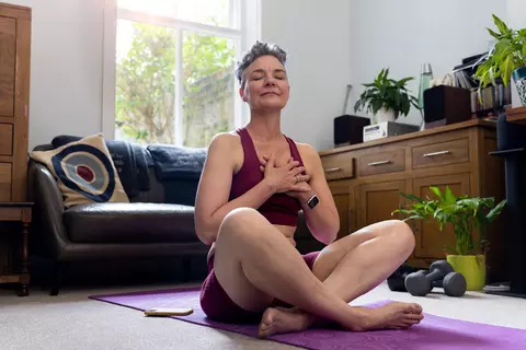 Frau mittleren Alters sitzt auf einer Yoga-Matte und atmet