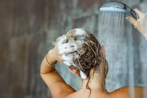 Frau duscht und spült Shampoo von Ihren Haaren runter
