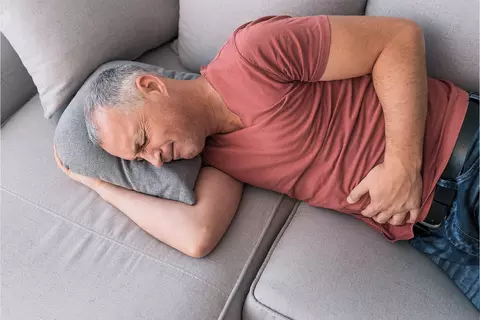 Mann liegt mit Bauchschmerzen auf der Couch