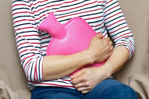 Frau hält sich eine Wärmeflasche an den Bauch