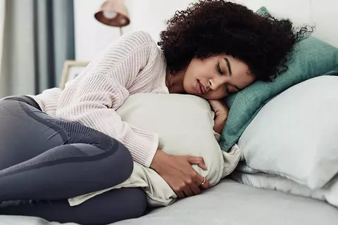 Frau liegt mit Menstruationsschmerzen im Bett