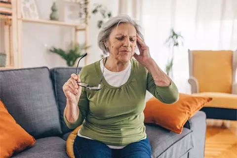 Ältere Dame ist schwindlig und setzt sich auf die Couch