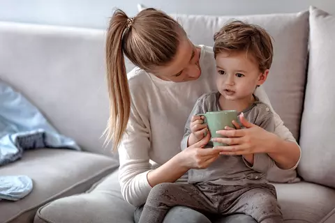 Kind trinkt etwas aus der Tasse auf dem Schoß der Mutter