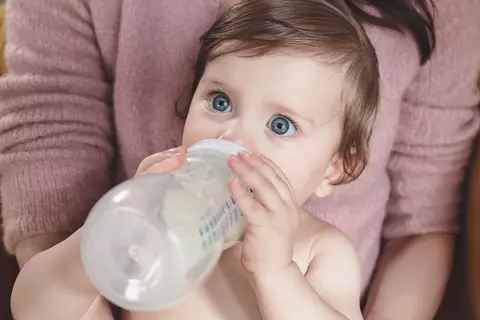 Baby sitzt bei der Mutter auf dem Schoß und trinkt aus einem Fläschchen