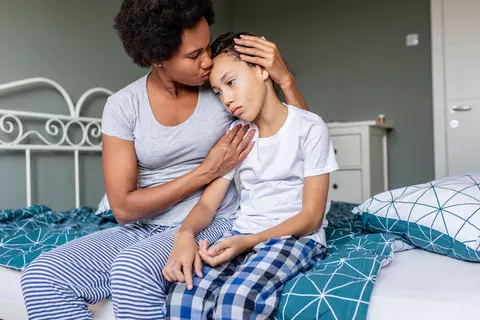 Mutter sitzt mit Kind auf dem Bett und tröstet es