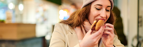Frau isst eine Bratwurst im Brötchen