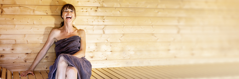 Frau sitzt lachend in der Sauna
