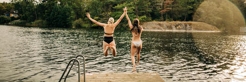 Zwei Frauen springen vom Steg aus ins Wasser