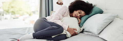 Frau liegt mit Menstruationsschmerzen im Bett
