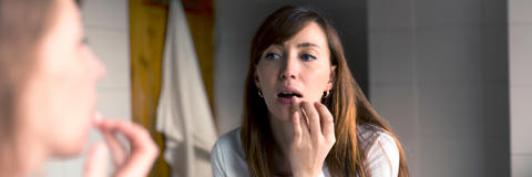Frau schaut sich im Spiegel an und fasst sich an die Lippe
