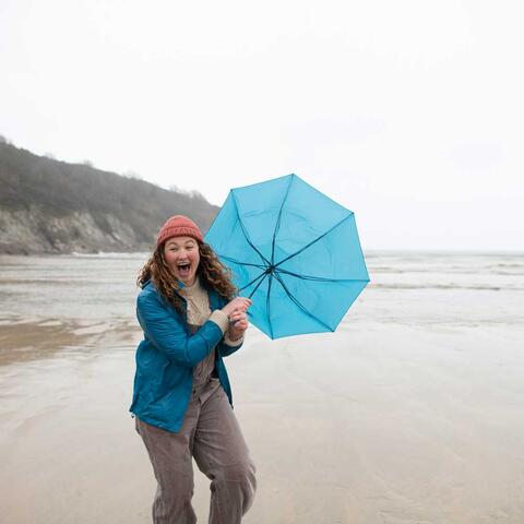 Frau läuft mit einem Regenschirm an einem stürmischen Strand entlang