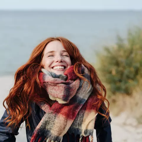Frau lachend am Strand mit Schal