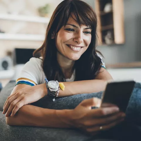 Frau sitzt auf der Couch und schaut ins Handy