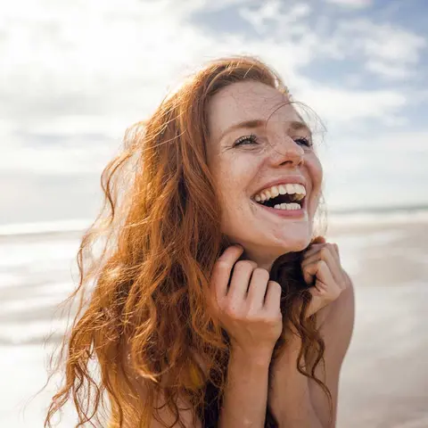 Junge Frau am Strand fasst sich in die Haare und lacht