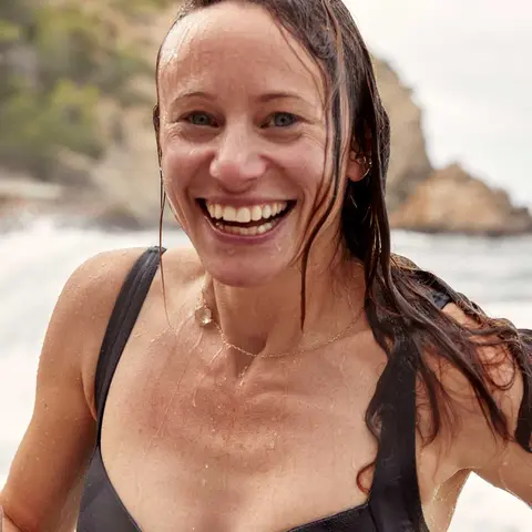 Frau kommt lachend aus dem Meer an den Strand gelaufen