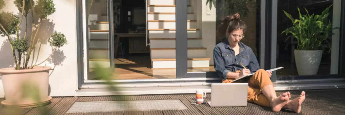 Frau sitzt mit dem Laptop auf der Terrasse