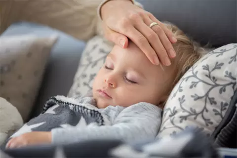 Dem schlafenden Baby wird eine Hand auf die Stirn gelegt