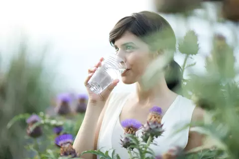 Frau trinkt im Garten ein Glas Wasser