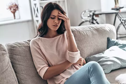 Frau sitzt mit Kopfschmerzen auf der Couch