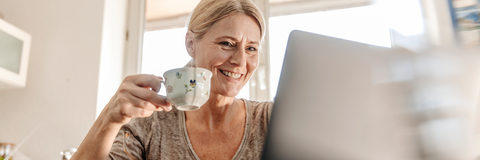 Frau sitzt mit Kaffeetasse am Laptop