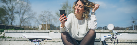 Frau sitzt draußen mit dem Handy