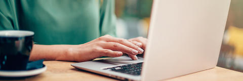 Frau sitzt mit Kaffee am Laptop