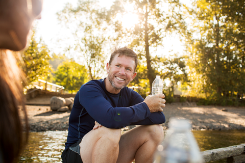 Mann sitzt mit einer Flasche Wasser auf einem Baumstamm