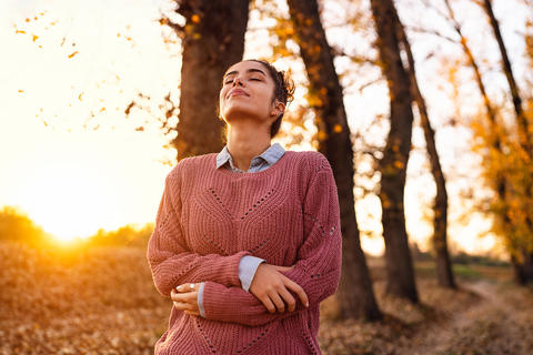 Frau spaziert durch eine herbstliche Landschaft und atmet tief ein