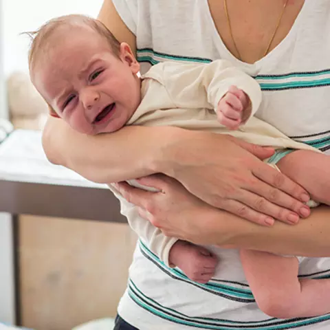 Eine Mutter mit Baby, hält das Baby im Fliegergriff, weil dieses unter starken Blähungen leidet.