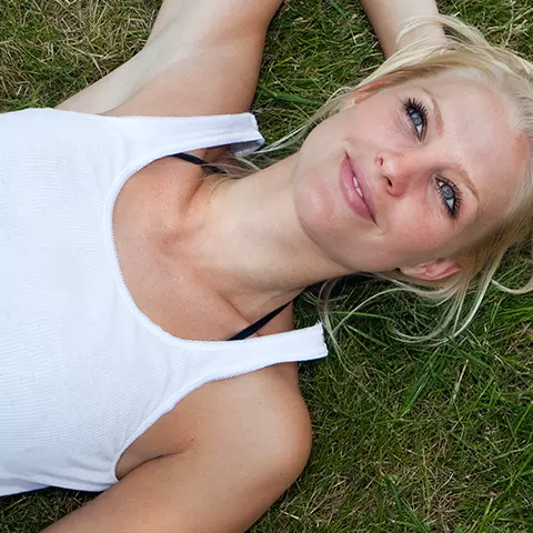 Eine junge Frau liegt auf der Wiese und hat ihre Bauchbeschwerden (Blähungen) im Griff.