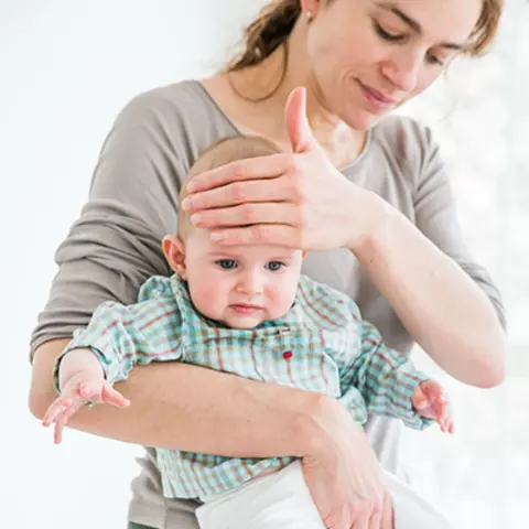 Eine Mutter mit einem erkältetem Baby macht sich auf dem Weg zum Arzt.