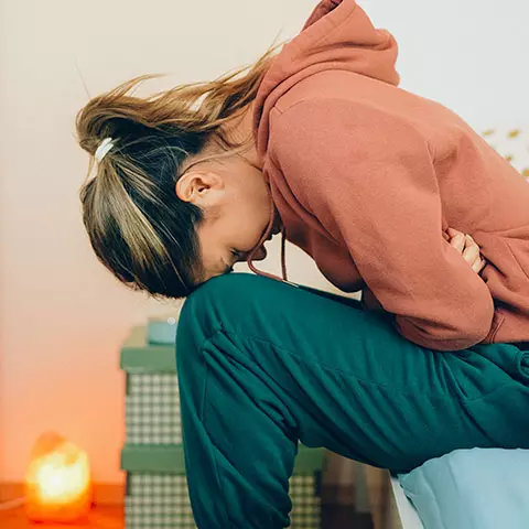 Frau krümmt sich mit Schmerzen auf dem Bett