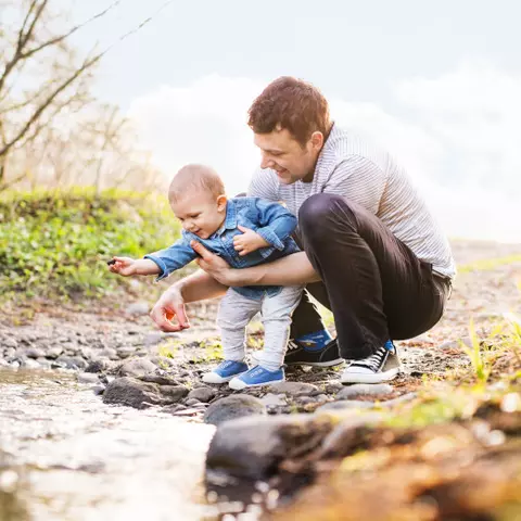 Vater spielt mit dem Baby draußen am Wasser